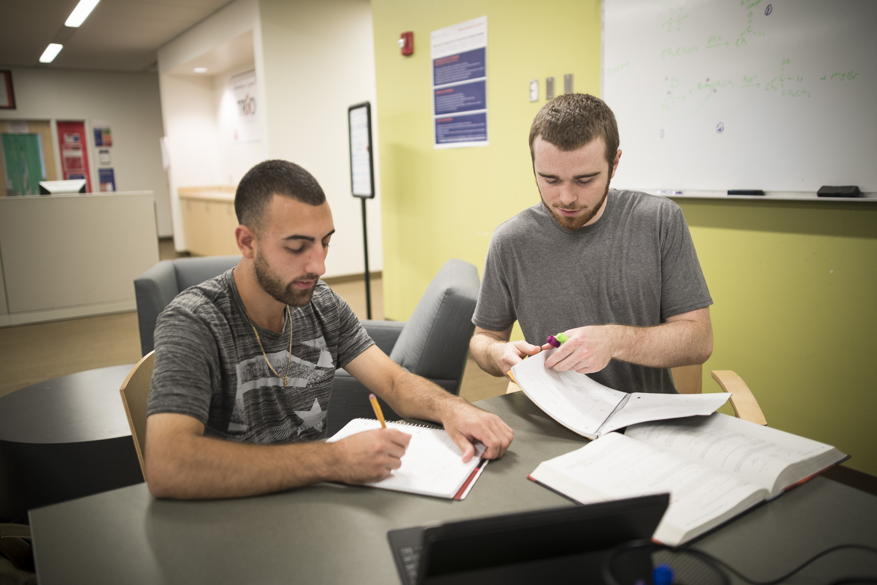 Two male students sit together in the library to study for a paper.