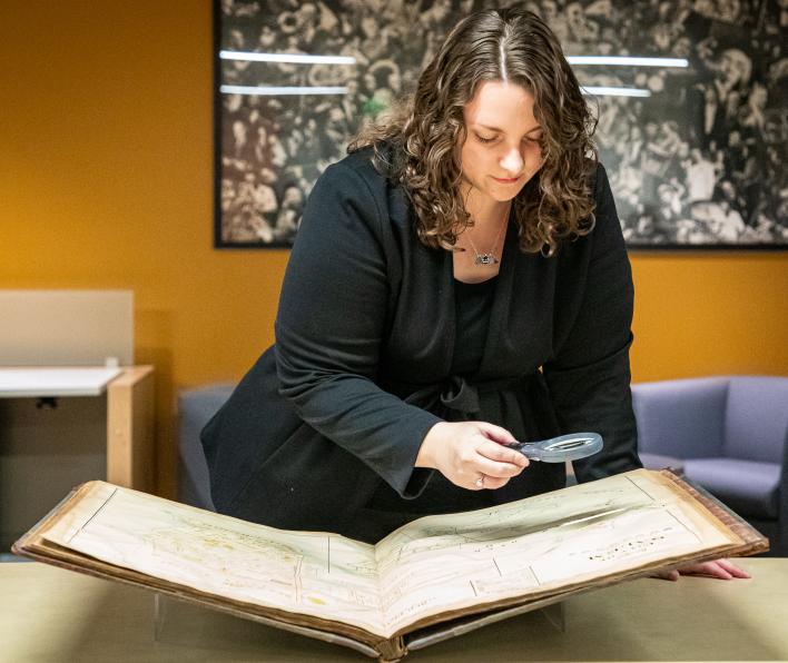 Jen Ratliff, 2018 graduate at Salem State, uses a magnifying glass to look at a historical map of Salem in the Salem State Archives.