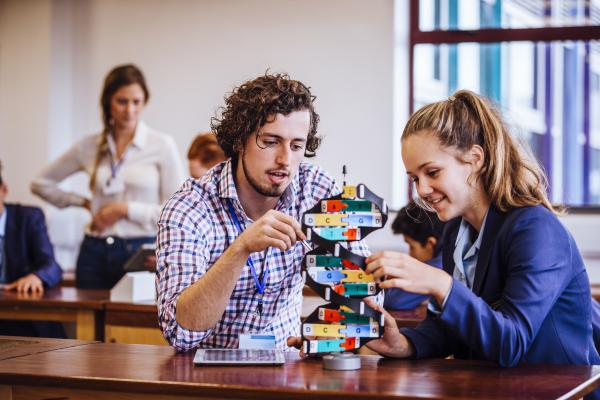 A teacher and a student sit at a wood table looking at a DNA block puzzle.