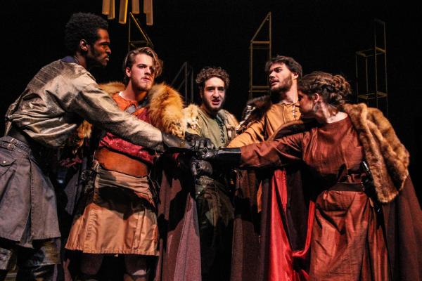Macbeth Theatre Photo: A group of men in costume huddle together and touch hands.