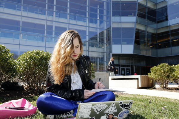 Girl sits in the quad with her laptop to register for tutoring. 