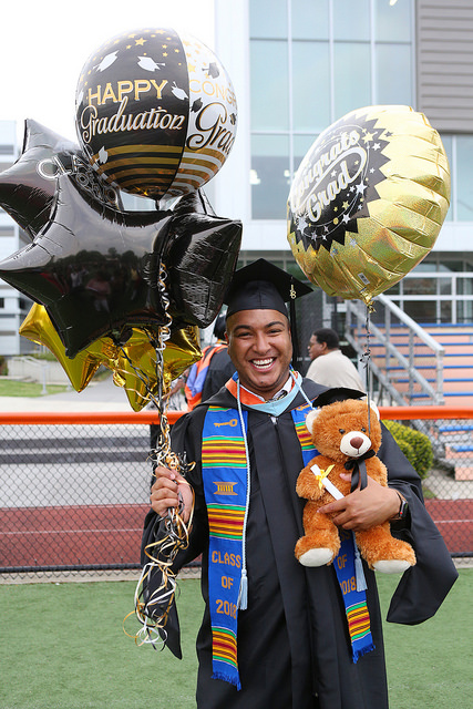 A graduate celebrates commencement with balloons on the soccer field