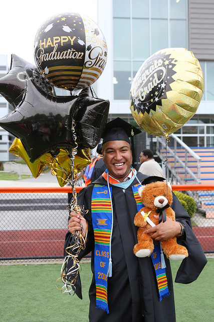 A graduate celebrates commencement with balloons on the soccer field