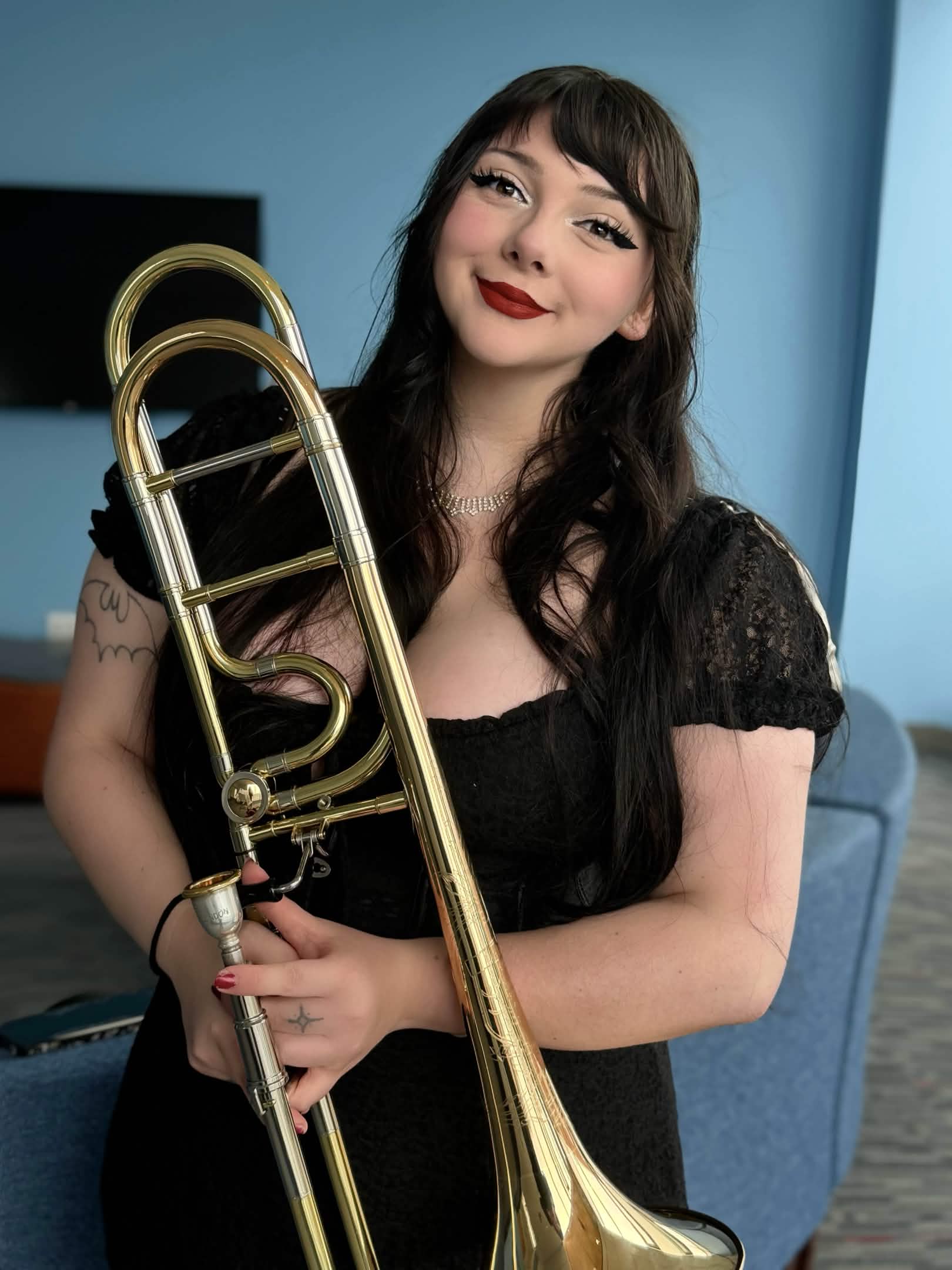 Ava O'Brien holding trombone standing in front of a blue wall