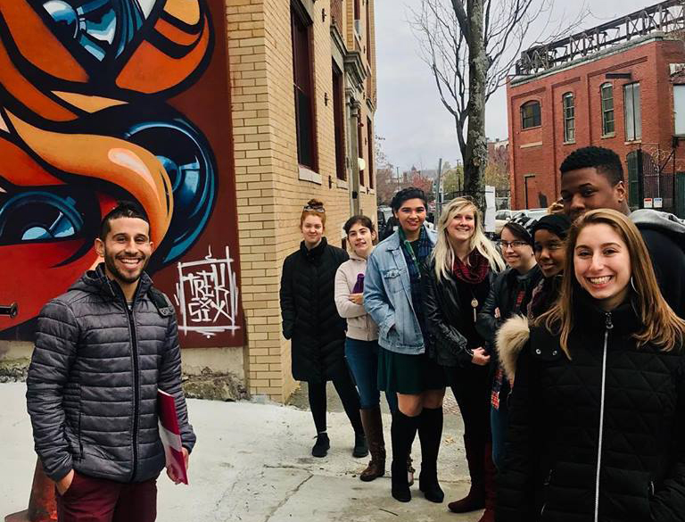 A group of students on a city block in front of a mural