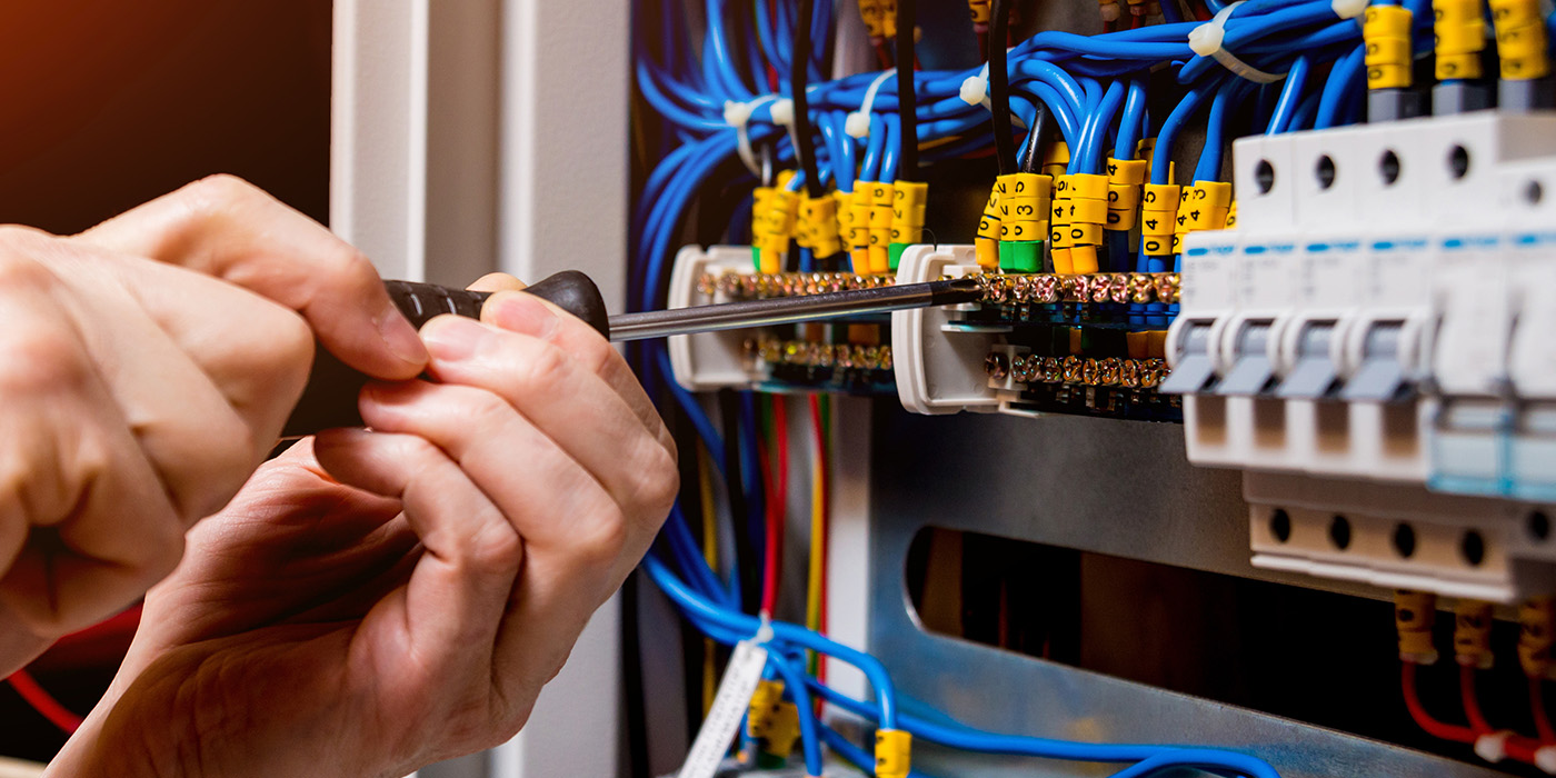 Close up of someone using a screwdriver on an electrical panel wiled with blue wiring