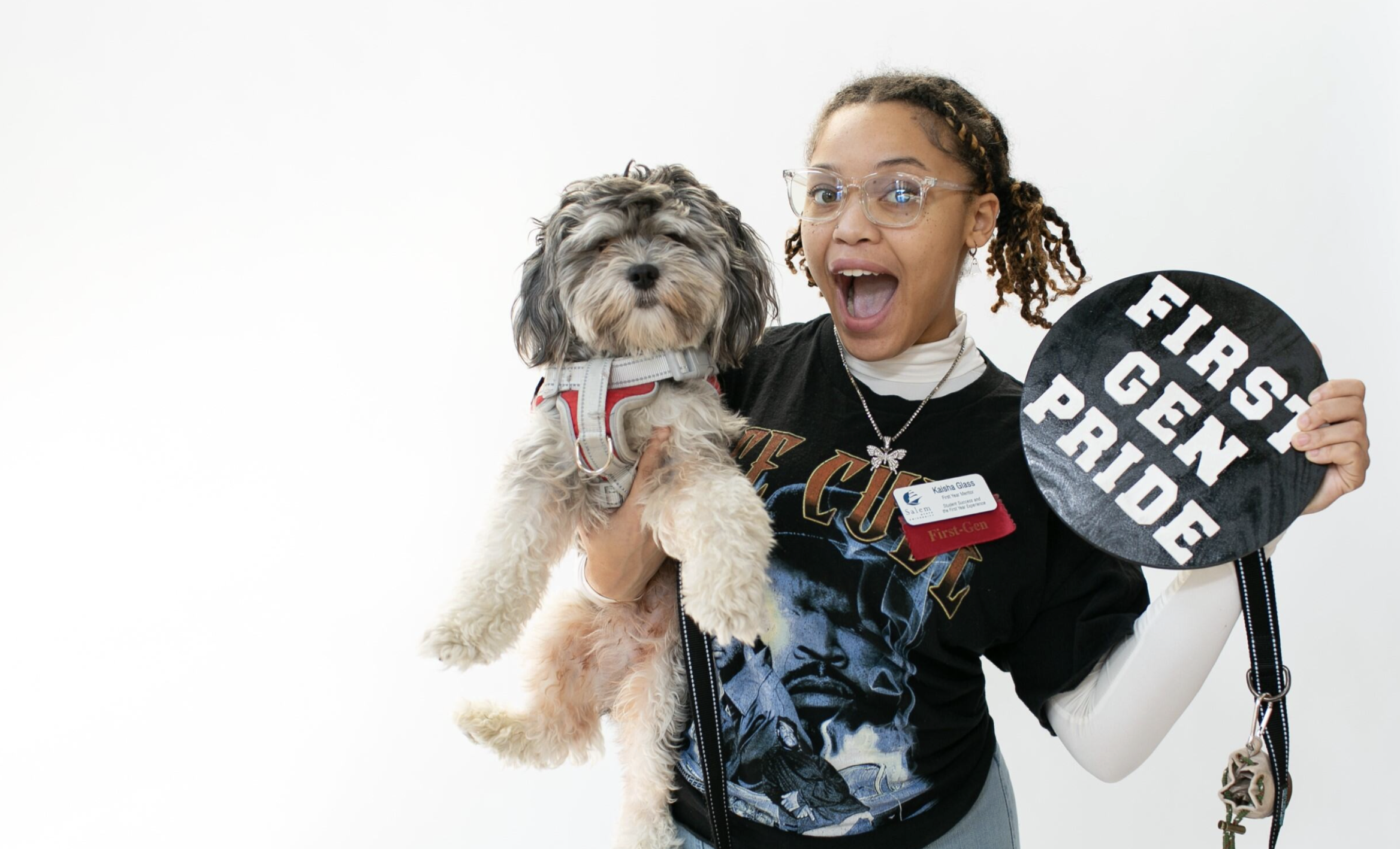 A Salem State first-gen student holds a dog in one hand, and a "first gen pride" sign in the other hand