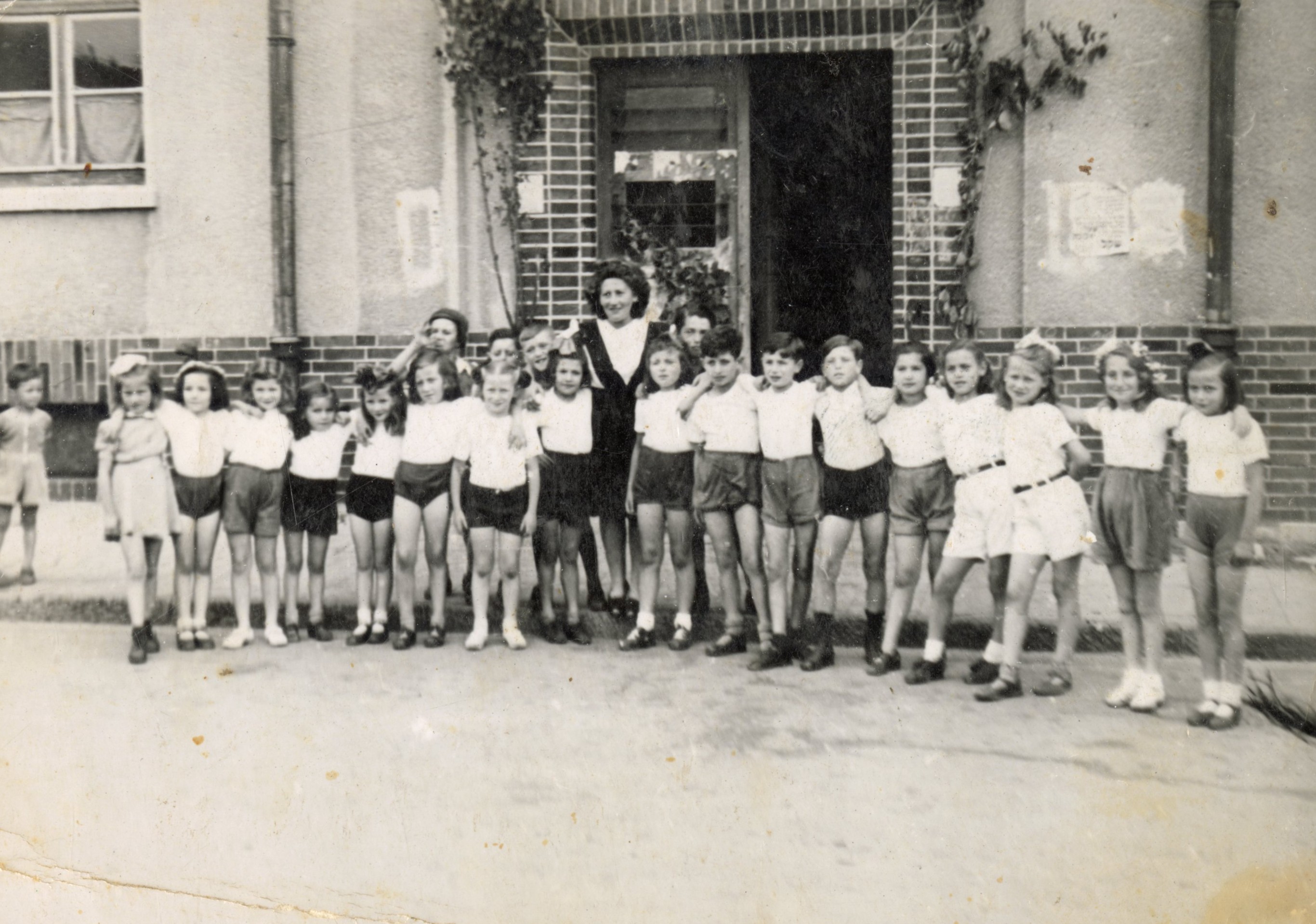 A group of children stand with an adult in an old black and white photo.