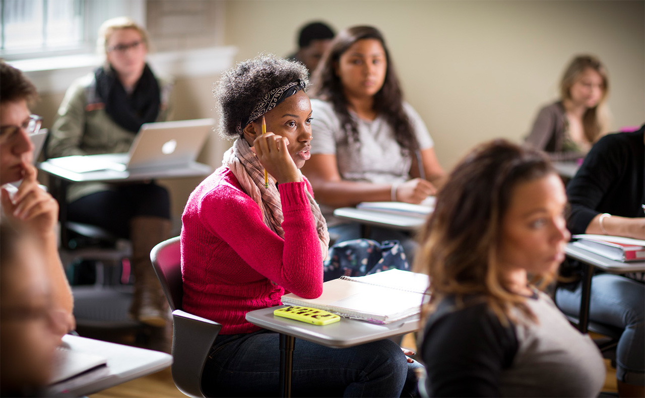 A girl sits at her desk answering the question of her professor. 