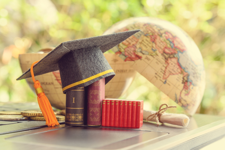 Graduation cap or hat, certificate or diploma, mini text books on a laptop computer, a half world glob