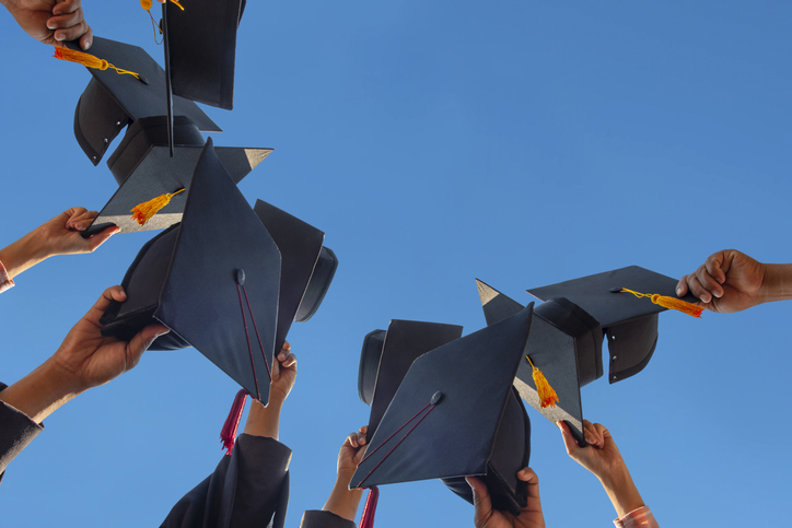 Hands holding graduation caps up against a blue sky.