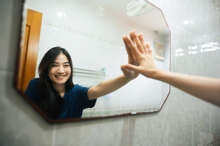An Asian woman touches her hand's reflection in the mirror