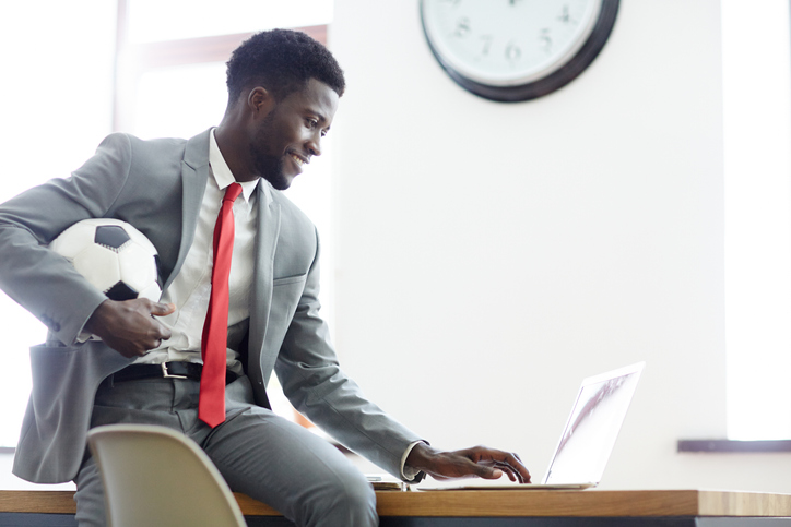 Fan of soccer with ball on his laptop while wearing a suit and tie.