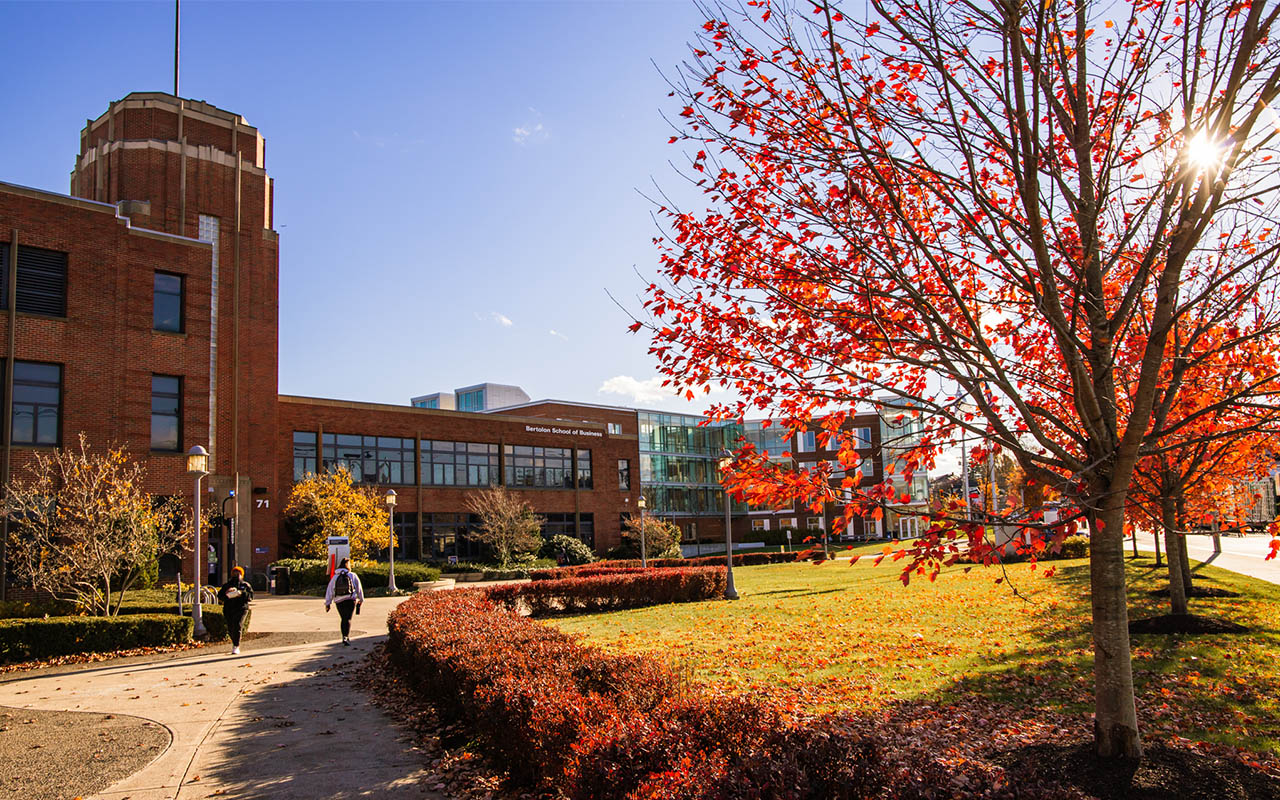 Students walking across Salem State University’s Harrington (Central) Campus on a sunny fall day, with red and orange foliage in front of the Bertolon School of Business