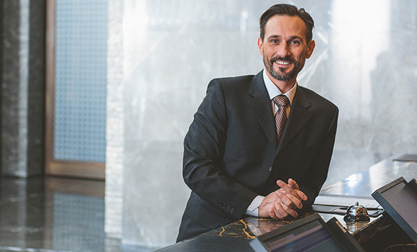 A smiling hotel manager leans on a lobby counter