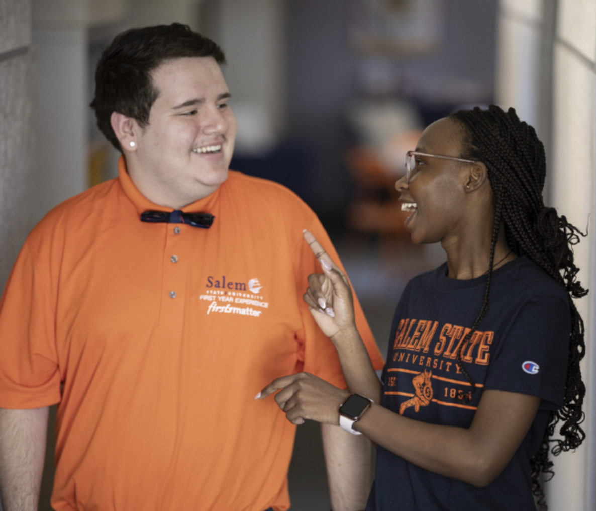 Two people walk and talk. They wear Salem State branded outfits. 