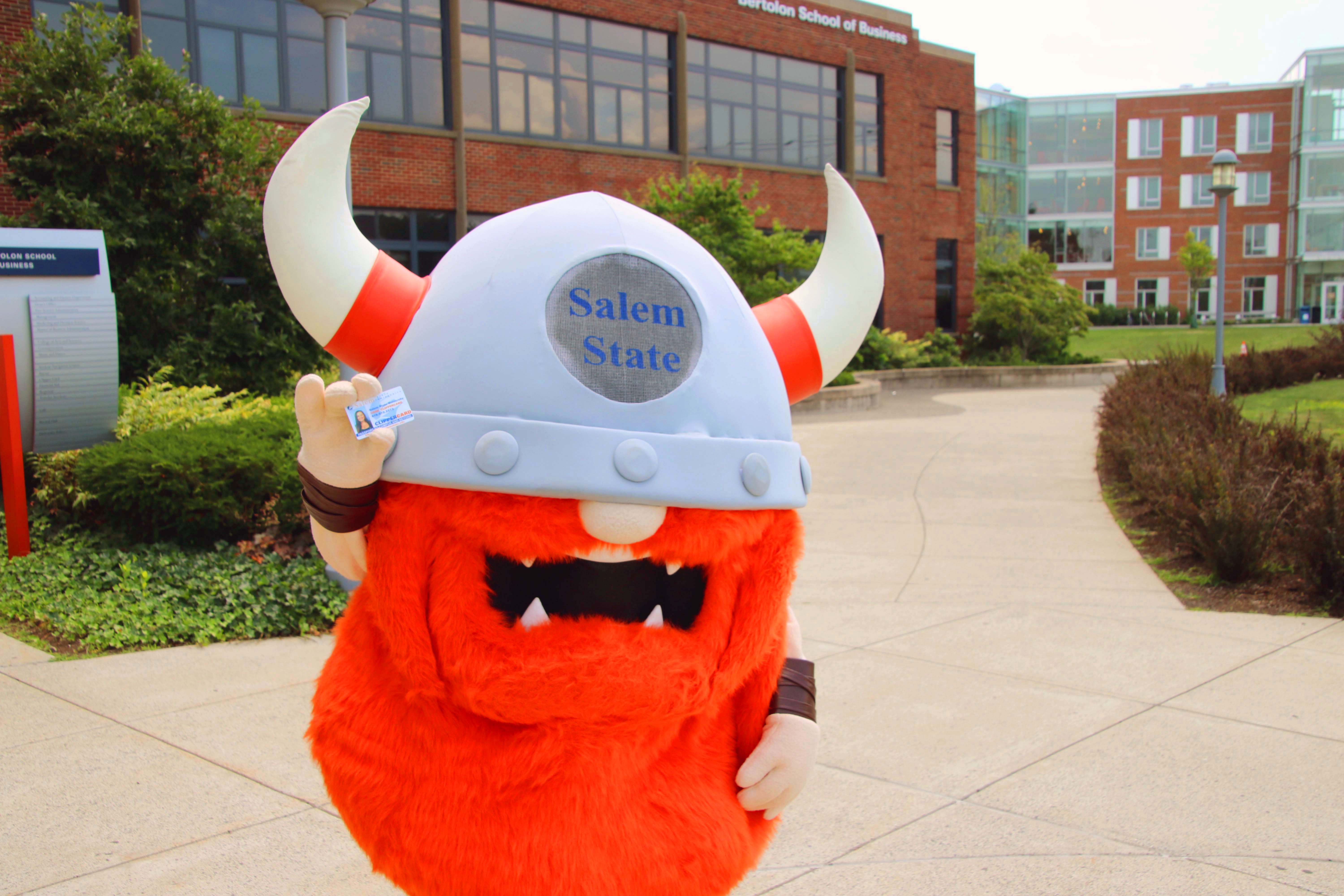 Superfan stands in front of the Bertolon School of Business holding a ClipperCard. 