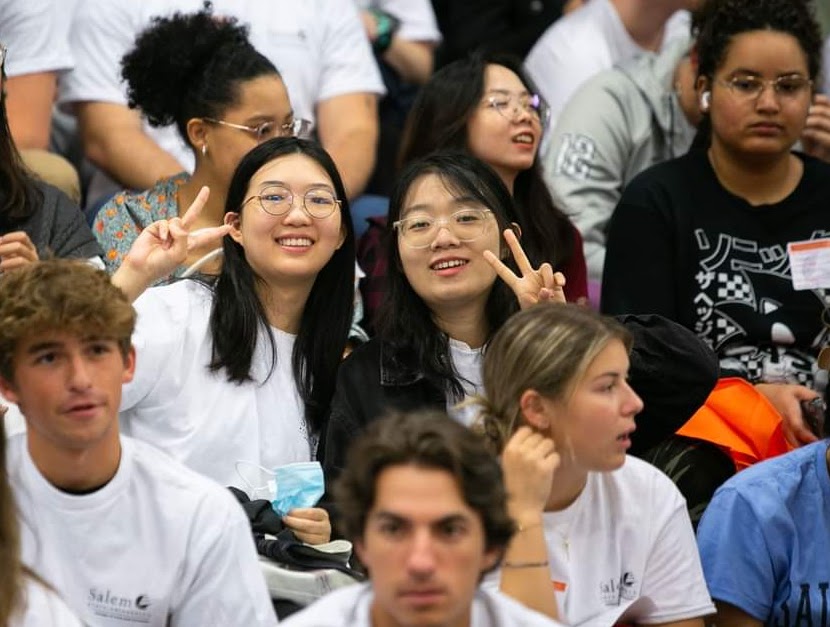 Two international students smile and do a peace sign. 