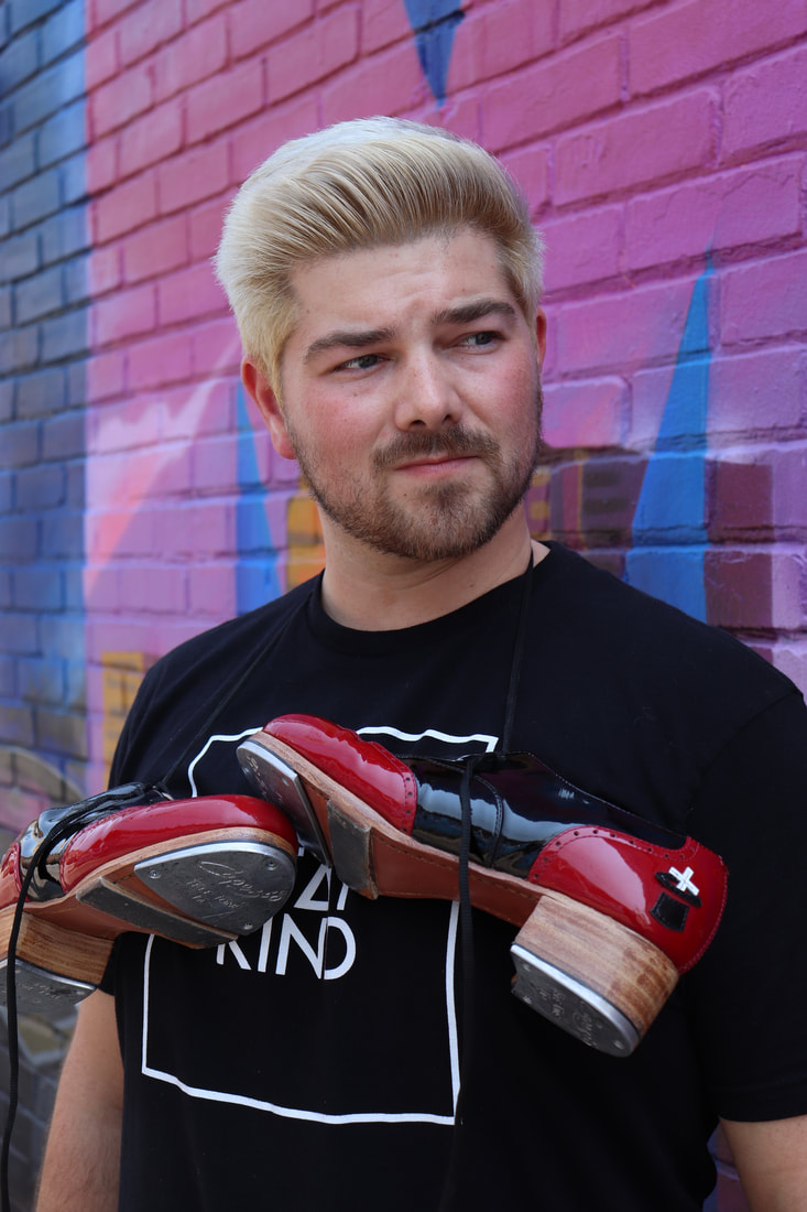 Man with spiky blond hair, black shirt and tap shoes hanging around his neck