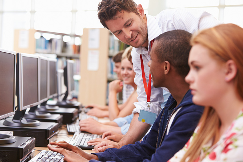 A librarian helps teenage students at computers in a library