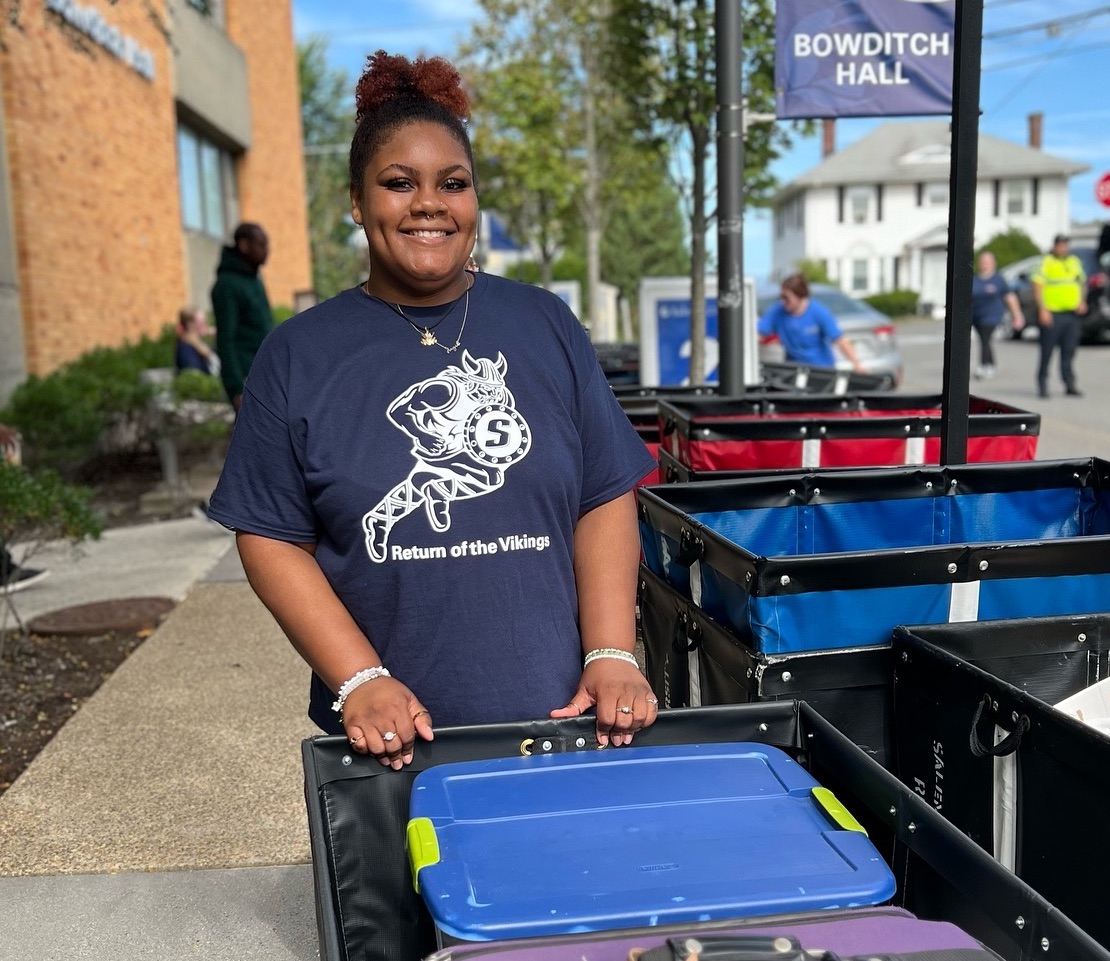 A smiling student with a move-in cart outside Bowditch Hall during move-in weekend