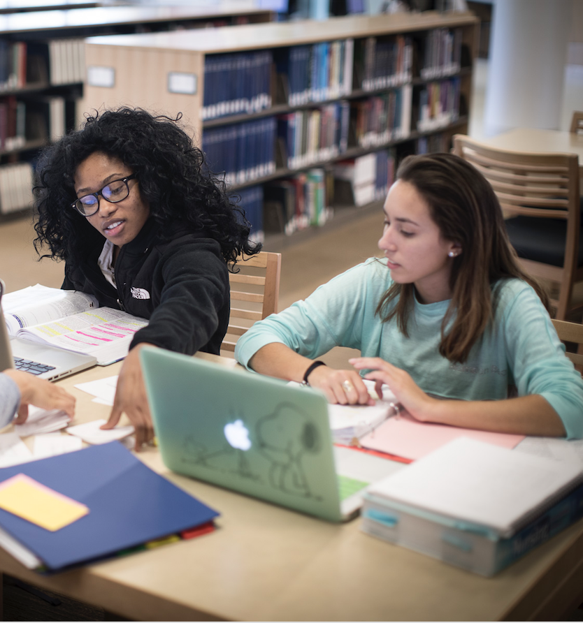 Three girls sit in the library with flash cards to study.