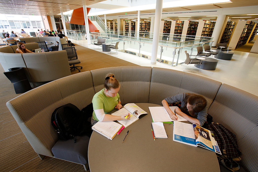 wide-angle view of 2 students working on table sitting on a long round couch that curves around half of the table