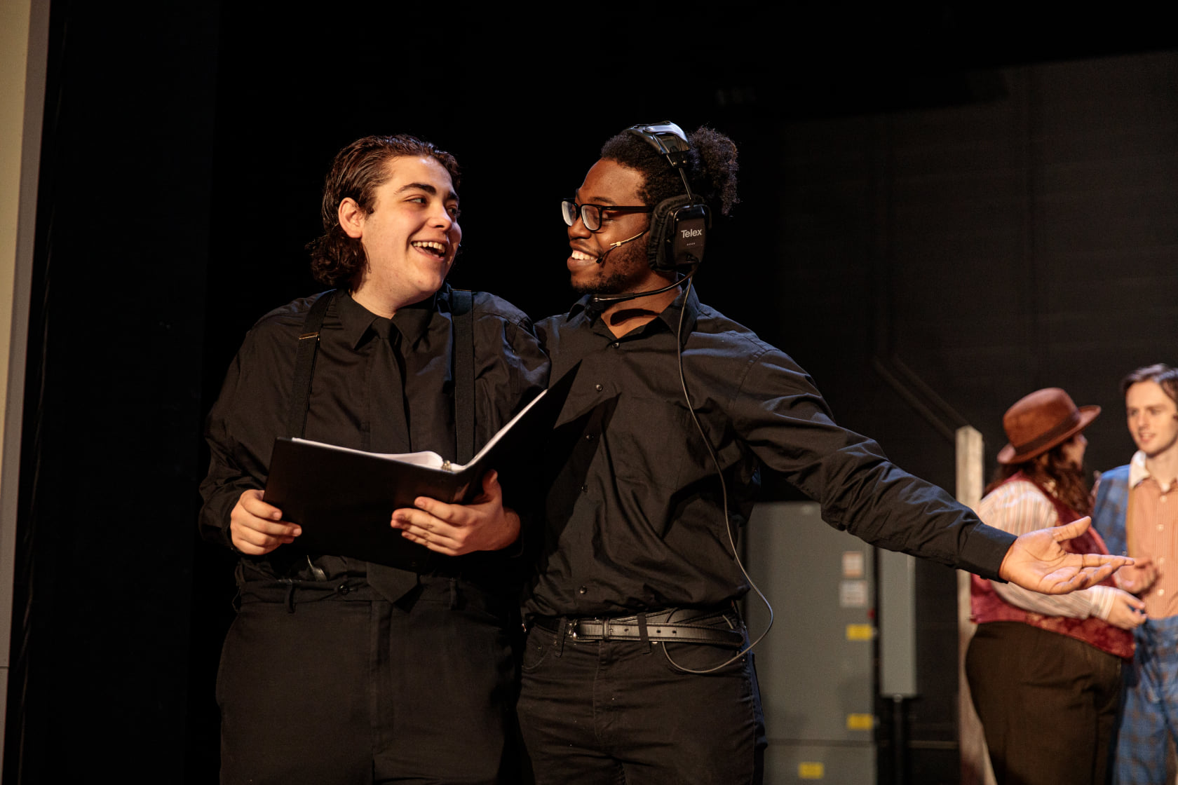 Rehearsal for a play; one actor is holding a binder with a script and a technician has a headset on next to him.