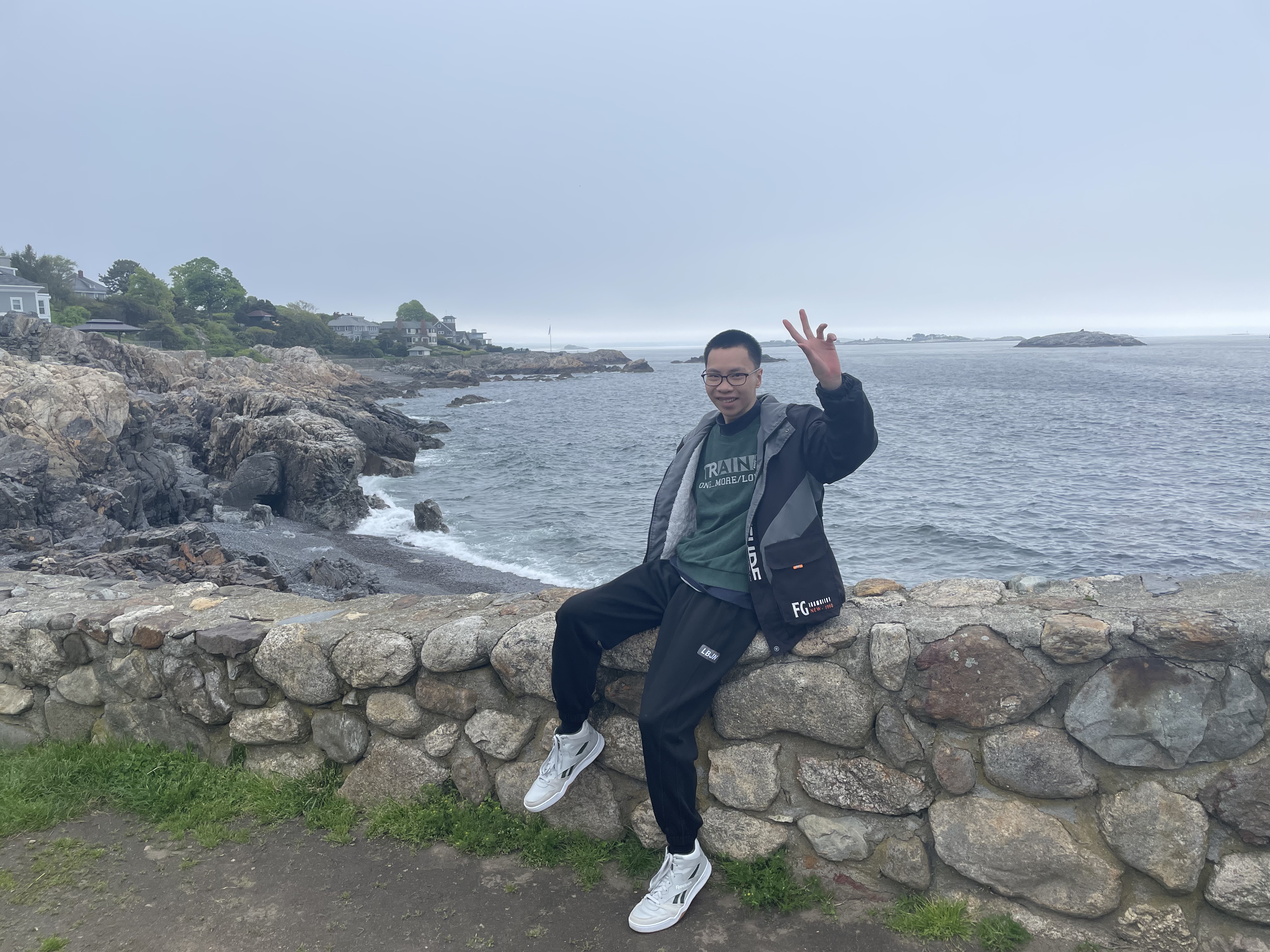 Zixuan Yu sits on a stone wall by the water