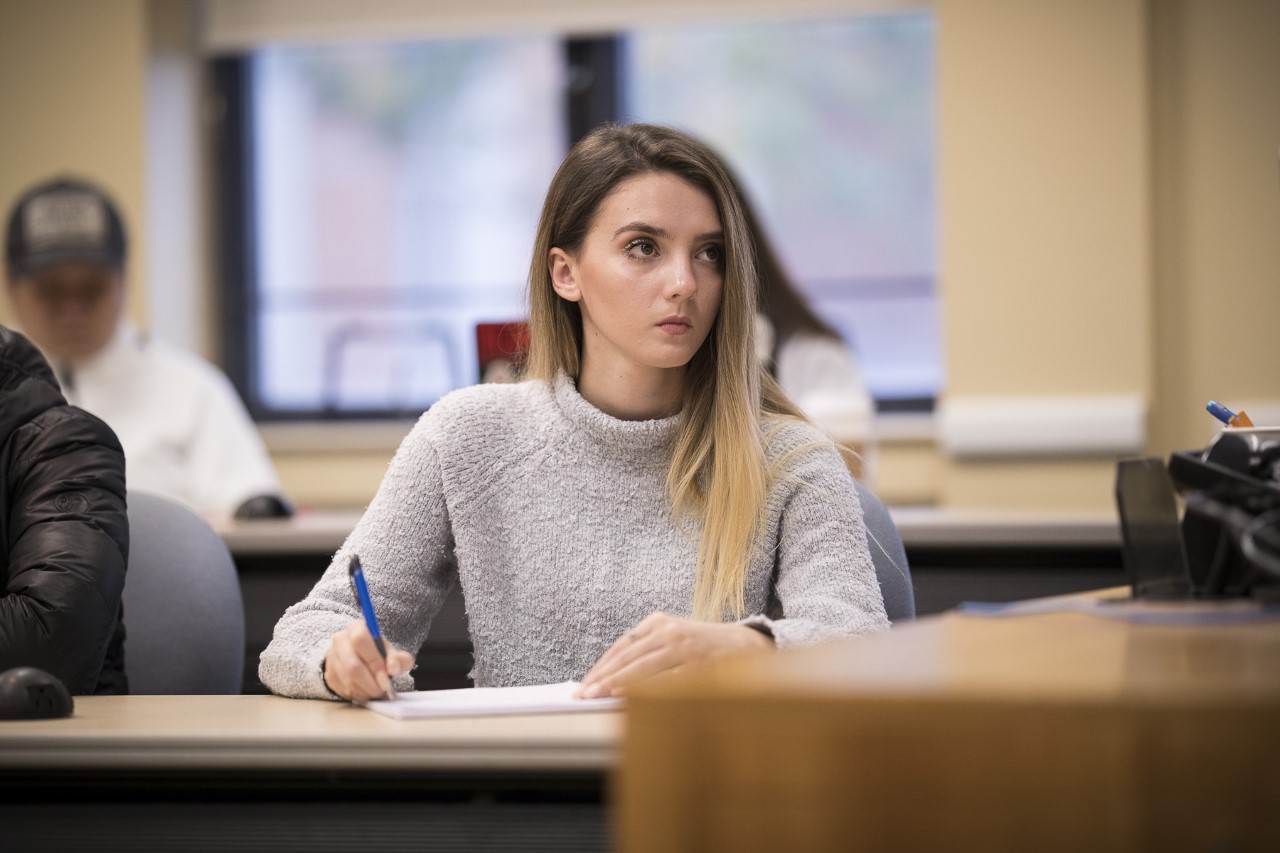 Student at in a classroom table listening and taking notes