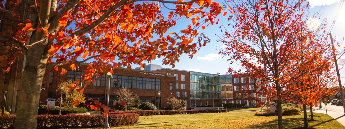 The façade of the Bertolon School of Business is framed by trees with red leaves.