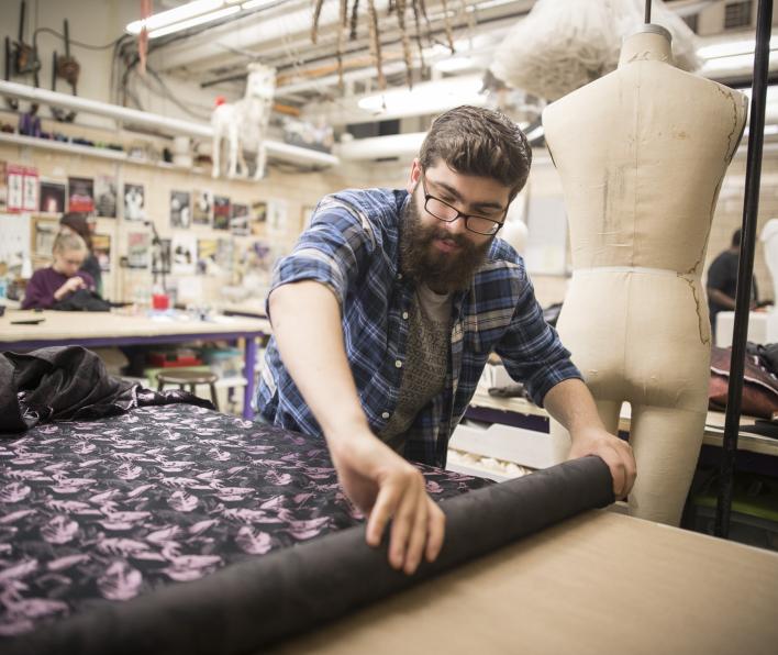A person rolls out fabric in front of a mannequin while designing costumes.