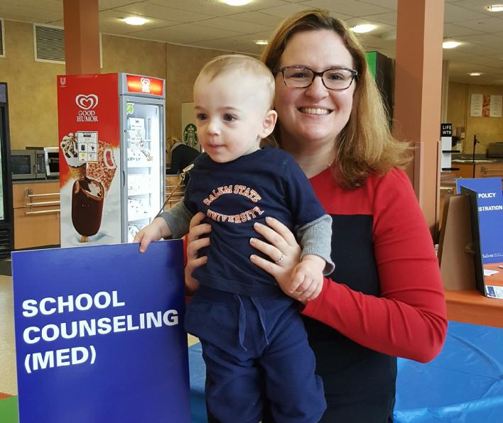 Dr. Laurie Dickstein-Fisher posing with her 1-year old son by the sign advertising the School Counseling Open House