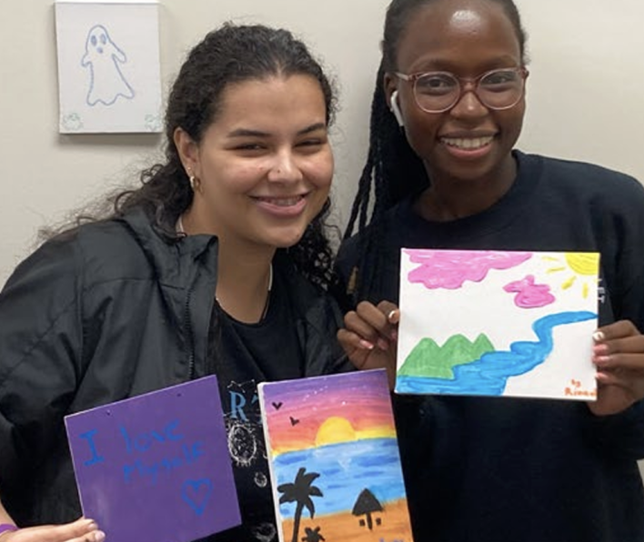 Two woman hold up paintings 