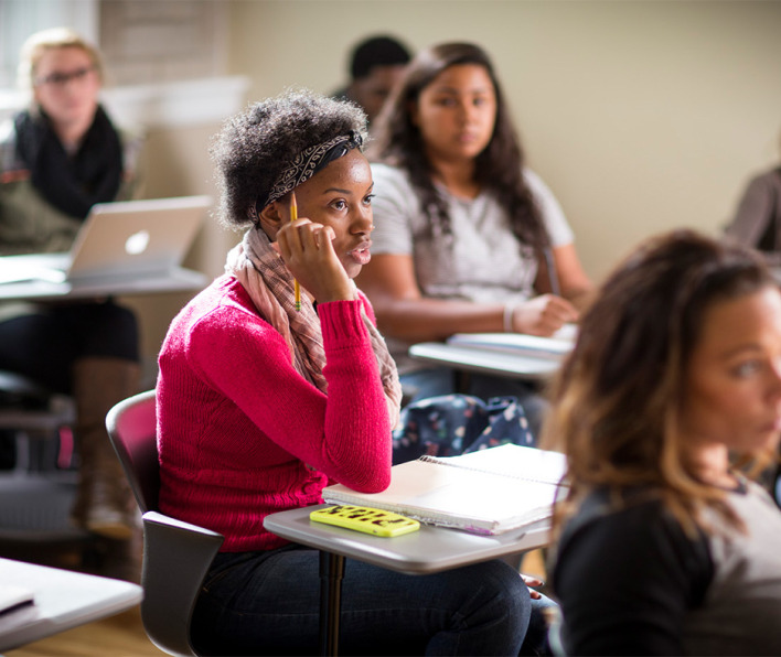 A girl sits at her desk answering the question of her professor. 