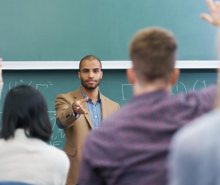 A male professor at the front of the room calling on a student