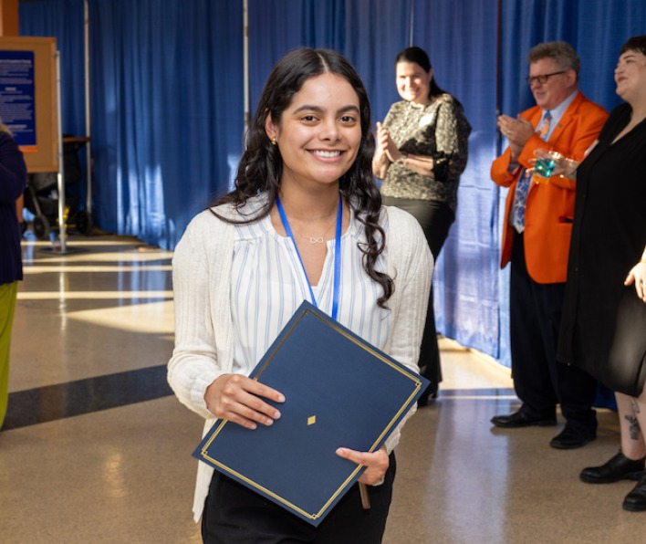 A smiling student with an award at Research Day