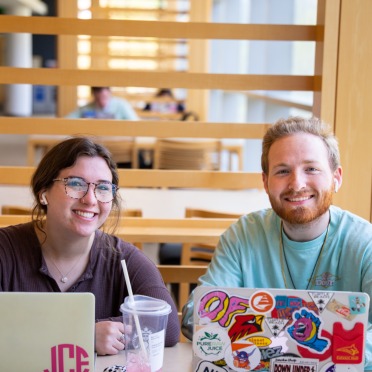 Two students sit together at laptops in the library