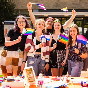 A group student stand in front of the Ellison Campus Center each holding a unique pride month flag