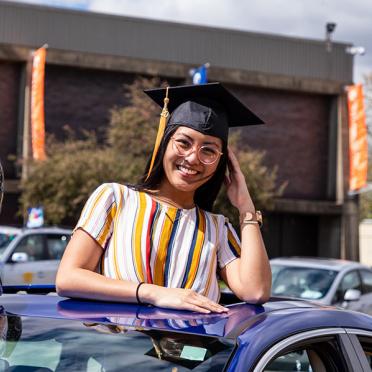 A 2020 graduate smiles from the sunroof of her car in front of the Gassett Fitness Center