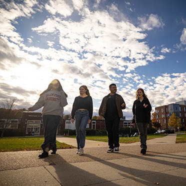 Four diverse students walk through Harrington (Central) Campus on a sunny fall afternoon with sun soaking the frame.