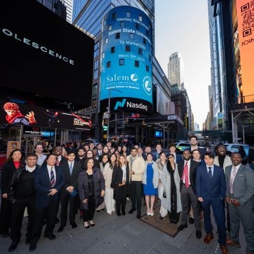 A group of BSB students in Times Square, NYC, with the Salem State logo displayed behind them on the Nasdaq screen.