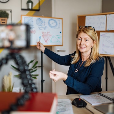 A professor in front of a phone camera on a tripod, pointing to a white board