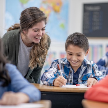 A student teacher smiling with an elementary student in the classroom