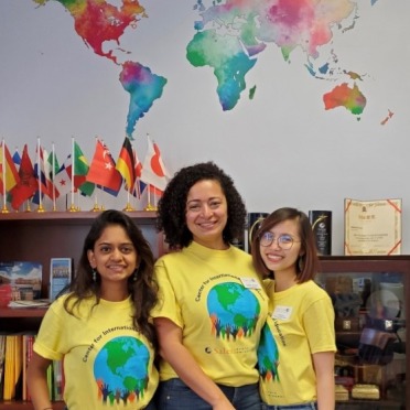 Three students stand under a watercolor map