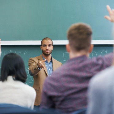 A male professor at the front of the room calling on a student