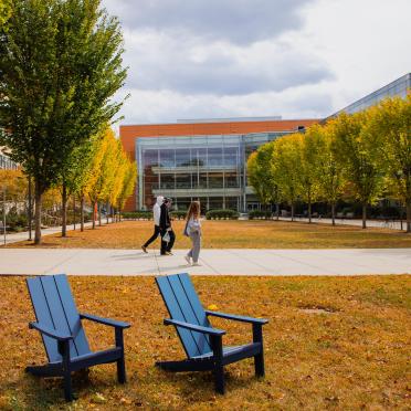 Blue chairs and students walking in front of the quad and Berry Library on a cloudy, fall day.
