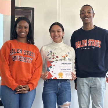 3 people smiling at camera. student in the middle is holding a certificate