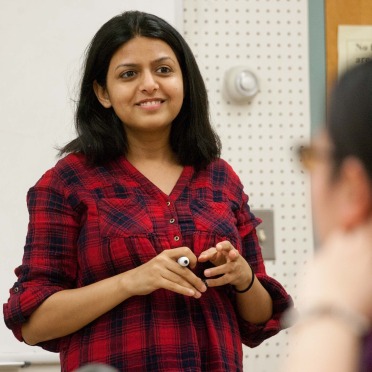 A female graduate school professor smiling at the front of the classroom