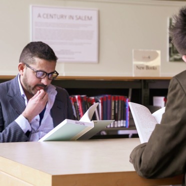 Two men read books across the table from one another in the Berry Library